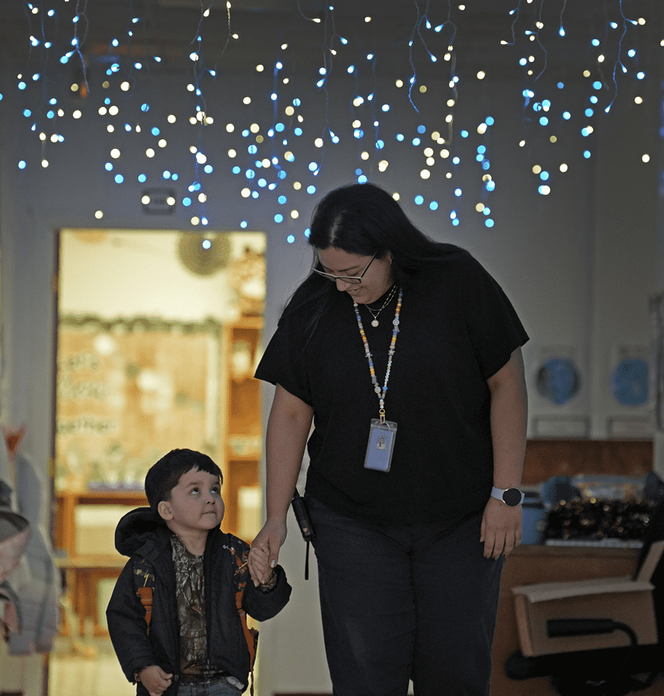 Woman holding a young boy’s hand as they walk indoors under blue string lights