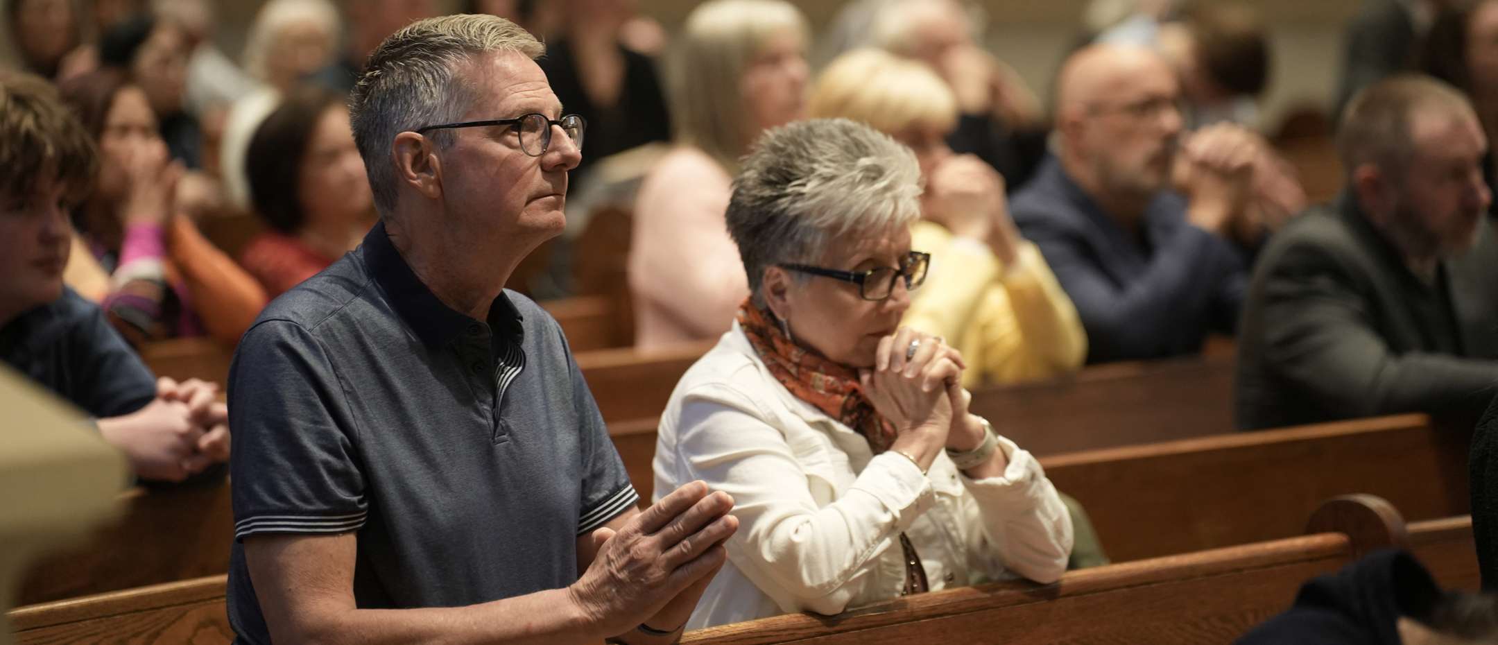 People seated in a church pew, praying during a service