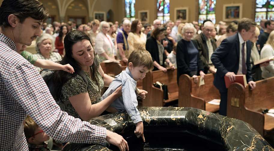 People gathered around a baptismal font in a church, with a child being held over the basin