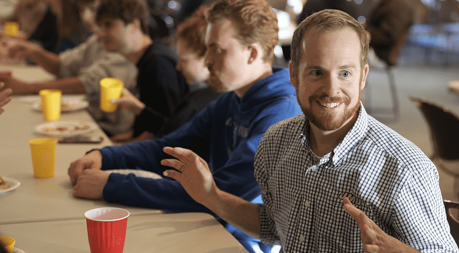 Man smiling and gesturing at a table during a group meal