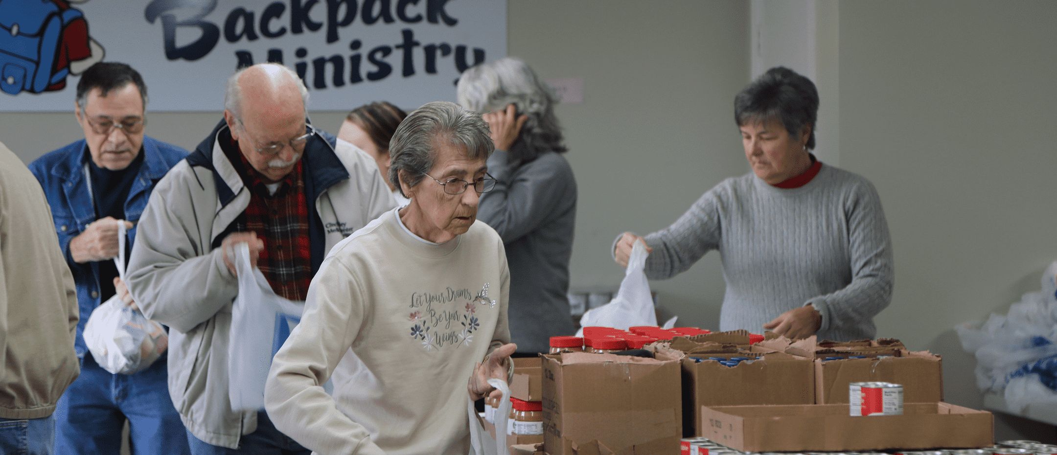 Volunteers packing food bags at a Backpack Ministry distribution table