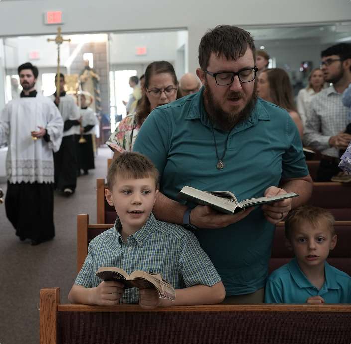 A man and two boys sing from hymnals during a church service