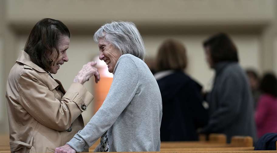 Two elderly women smiling and talking in a church or community hall
